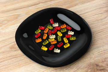 Jelly bears on a black plate. Multicolored sweets in a plate on a wooden table.