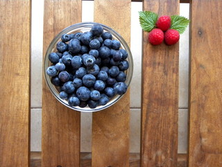 blueberries in a glass bowl and raspberries on a wooden table