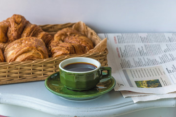 Traditional french breakfast: hot croissants and cup of coffee, paper on the white table