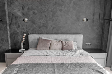 Grey bed in monochromatic bedroom with pillows and loft lamps on the wall.