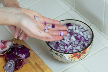 Hand tumbling diced red onion into small bowl of water