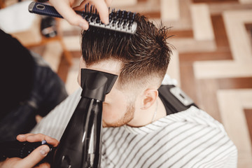 Close-up master Barber does hairstyle and styling with dryer hair to guy. Concept Barbershop