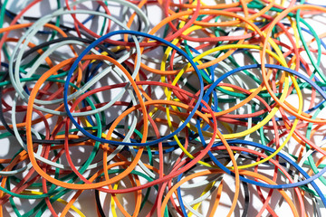 Many multi-colored rubber bands for money lie on a white surface.