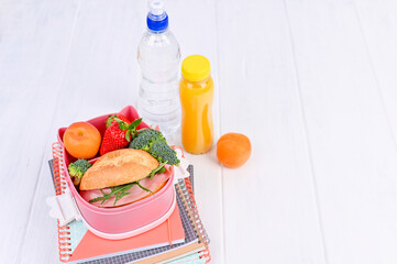 School lunch on a white wooden table. Lunch for the student and drink. Free space for text. Fruit, sandwich and books.