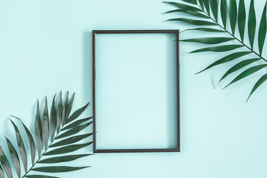 Summer composition. Tropical palm leaves, black photo frame on pastel blue background. Summer, nature concept. Flat lay, top view, copy space