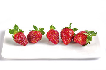 Ripe strawberry on white background. Three berries lie on a flat white plate.