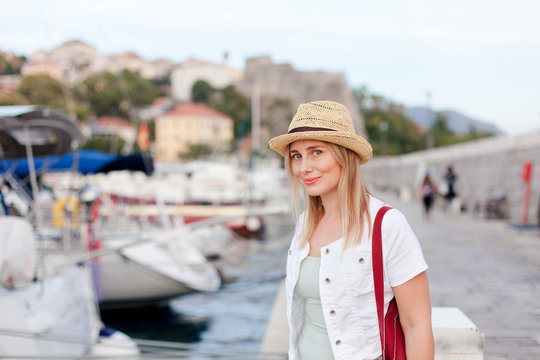 Woman traveler in yachts port near old town. Concept of student travel, summer vacation, solo female tourism, adventure, trip. Happy girl tourist stands on embankment in Herceg Novi, Montenegro.