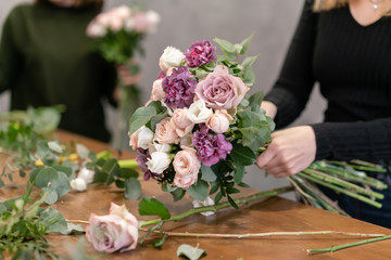 Close-up flowers in hand. Florist workplace. Woman arranging a bouquet with roses, carnation and other flowers. A teacher of floristry in master classes or courses