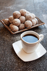 Czarna kawa w białej filiżance obok tacy z mini pączkami posypanymi cukrem pudrem