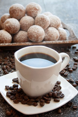 Black coffee in a white cup next to a tray with mini donuts sprinkled with powdered sugar