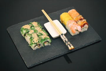 Japanese food restaurant, sushi maki gunkan roll plate or platter set. Copy space, chopsticks, ginger, soy sauce, wasabi. Sushi served on black stone. Top view.
