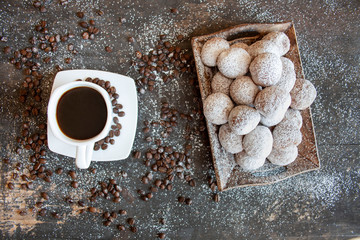 Czarna kawa w białej filiżance obok tacy z mini pączkami posypanymi cukrem pudrem © Monika