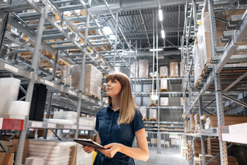 Wholesale warehouse. Beautiful young woman worker of store in shopping center. Girl looking for goods with a tablet is checking inventory levels in a warehouse. Logistics concept