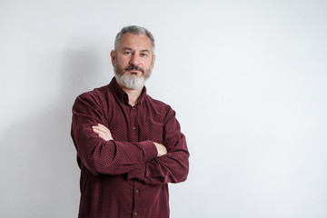 Half-length portrait of a serious gray-haired bearded man in a burgundy shirt on a white background