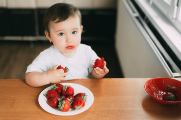 Little girl child in white t-shirt eating strawberries all smeared and dirty