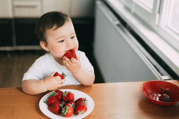 Little girl child in white t-shirt eating strawberries all smeared and dirty