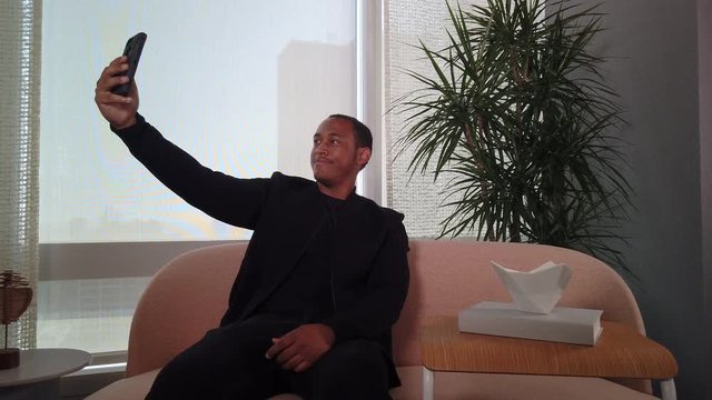 Happy African American Man taking selfies on cell phone while sitting on sofa.