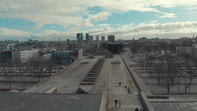 Large gray architectural complex or bridge with two staircases and walking people against blue cloudy sky and city buildings in early spring. Shot. Urban architecture