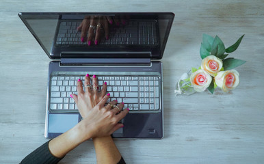 MANOS CRUZADAS SOBRE EL TECLADO DE UN LABTOP Y FLORES A SU LADO
