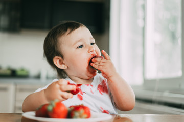 Little girl child in white t-shirt eating strawberries all smeared and dirty