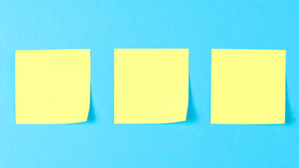 Blank yellow sticky notes on a blue background, concept of business work. Yellow memo stickers on blue wall. Mock-up