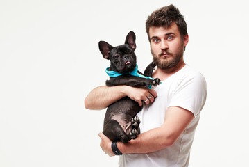 Hipster Bearded guy holding and hugging a nice French Bulldog dog in his arms with love and playing with him, against a white background
