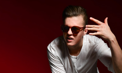 Obraz premium Elegant young handsome man in elegant casual dress and sunglasses in the studio on a red background.