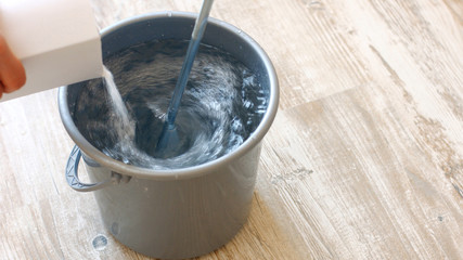 Builder knead glue for wallpapering. Pouring wallpaper paste in to a bucket of water and stirring with a stick. House repair concept.
