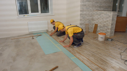 Men in the uniform laying laminate. Builders finishing house renovation. Repair service.