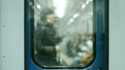 Blurred background people in the underground carriage. Passenger sitting in underground train, view through glass door. Modern city transport.