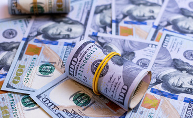 A roll of 100 dollar bills close-up on a pile of American dollars. Financial concept.