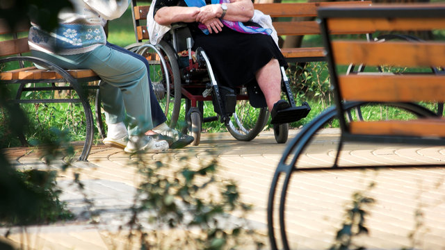 Old people talking sitting on bench outdoors. Disabled senior woman having coversation with her friends in the park.