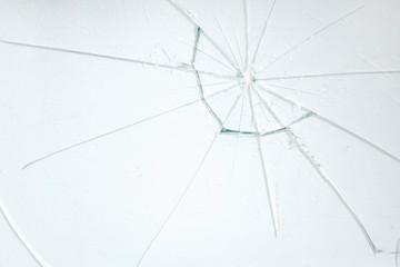A badly broken transparent glass on a white surface, with a web pattern of sharp shards.