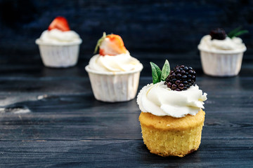 Cupcakes with whipped cream and strawberries and blackberry on old blue background. Festive party cakes for birthday, wedding.
