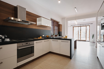 Elegant white and black kitchen with wooden accents and open space empty living room interior with floor to ceiling windows