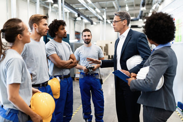 Corporate manager talking to group of workers while visiting a factory.