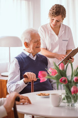 Smiling grandfather talking about his day schedule with a nurse in retirement home