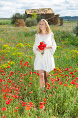 Obraz na płótnie Canvas Woman in white dress walking and holding bouquet of poppies plants