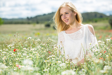 Naklejka na ściany i meble Young woman wearing white dress posing in fields with daisies flowers