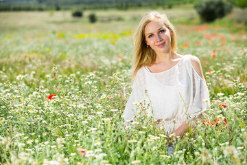 Young girl  in white dress  sitting in field of wild chamomile   flowers