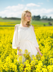 Naklejka na ściany i meble Young woman in yellow oilseed rape field posing in white dress