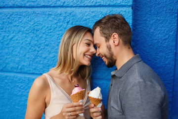 Happy couple in love eating ice cream and smiling on blue wall background