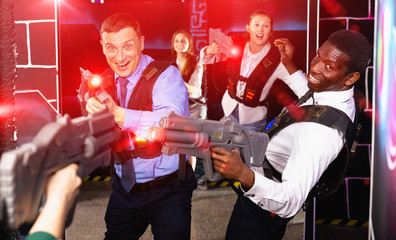 Men and women in business suits playing laser tag emotionally in