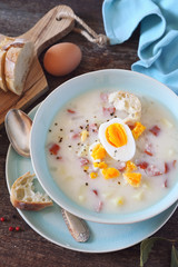 Traditional polish soup Zurek. Sour soup with sausage,  potatoes and eggs in ceramic bowl