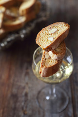 Italian cookies: almond cantuccini and glass of white wine on wooden background