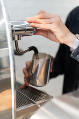 man holding steel coffeepot and brewing a fresh hot coffee into it with coffee machine in cofeeshop