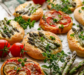 Mini pizzas with the addition of green asparagus, tomatoes, cheese and herbs, close-up. Vegetarian pizzas, delicious appetizer