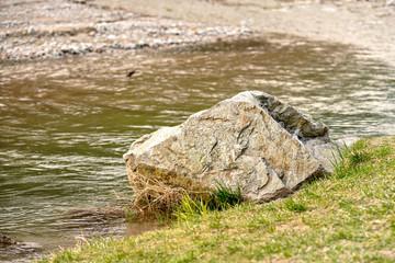 Large boulder rock on grass side of the river.