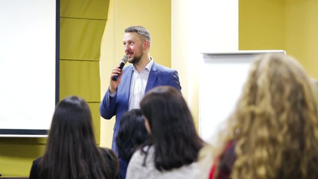 Executive leader is talking into the microphone at public seminar. Professional speaker teaching the audience during the conference.