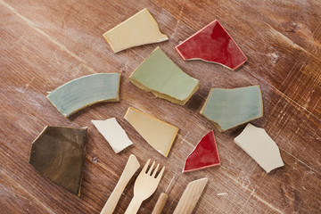 Close-up of colorful ceramic shards of broken plates and wooden sculpting tools on scratched table